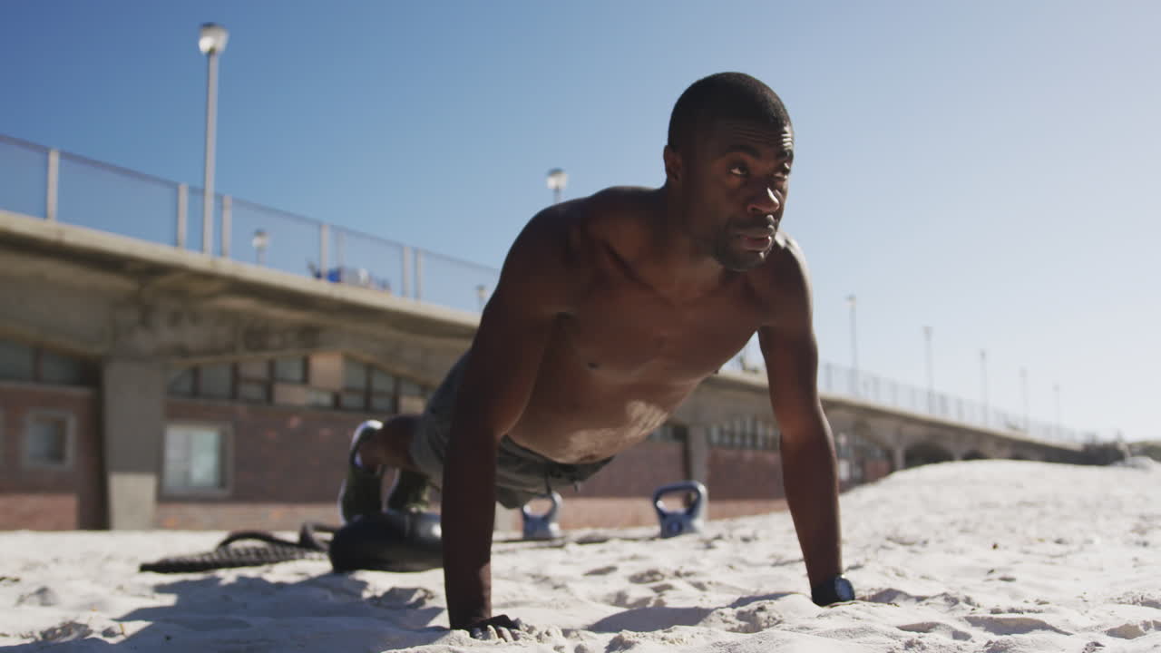 Uomo afroamericano concentrato che fa flessioni, allenandosi all'aperto sulla spiaggia.