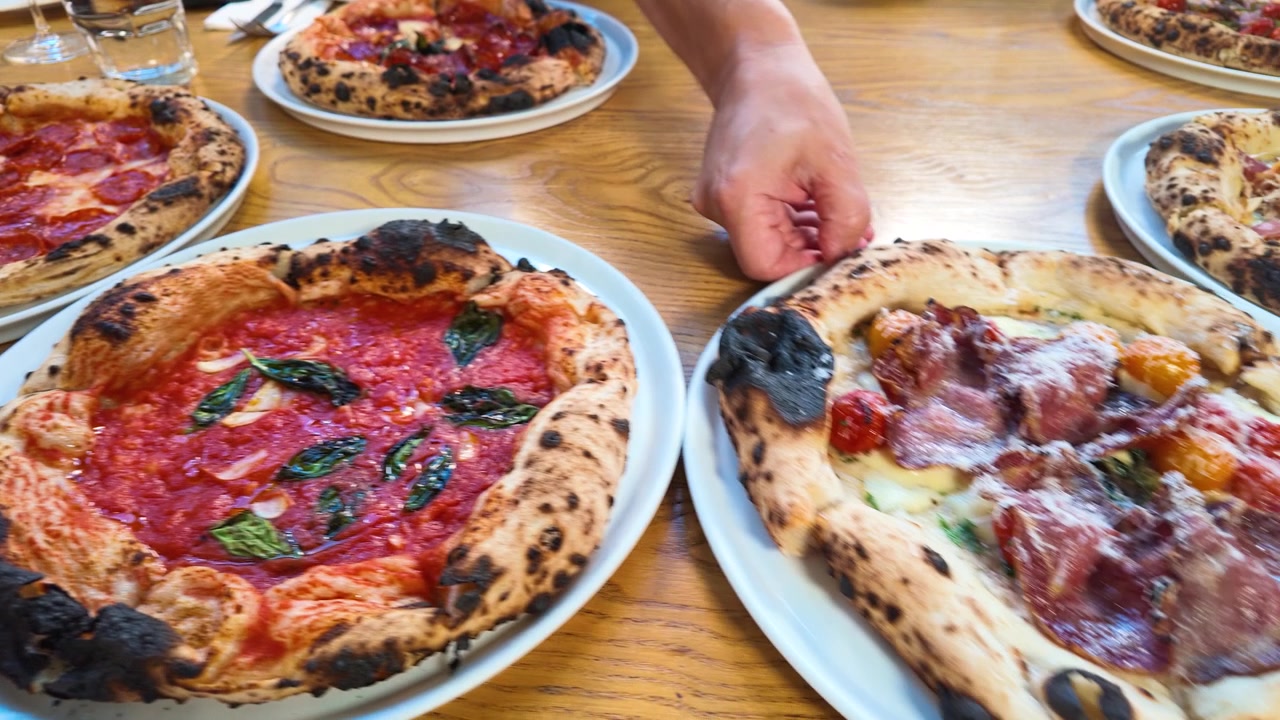 Camerieri posizionano varie pizze gourmet su un tavolo da pranzo in legno sotto una luminosa illuminazione interna.