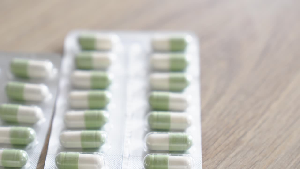 Close-up of green and white capsules in blister packaging on a wooden table. Concept of pharmaceuticals, healthcare, and daily medication use.