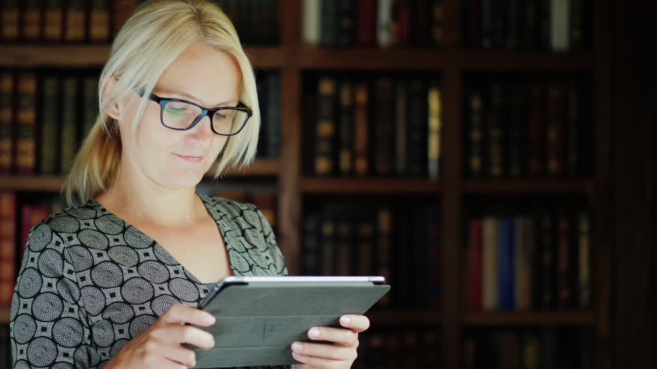 mujer con gafas usando una tableta junto a una estantería