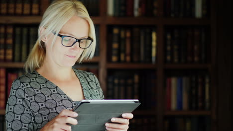 mujer con gafas usando una tableta junto a una estantería
