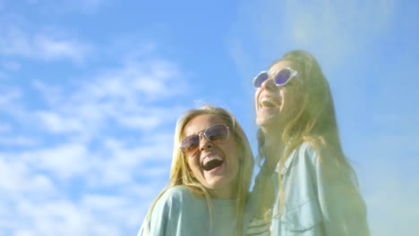 dos hermosas chicas felices se ríen y celebran el festival de holi polvo de colores volando detrás de sus espaldas. tienen mucha diversión.