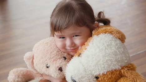 A-little-girl-hugs-plush-soft-toy-teddy-bears,-looking-at-camera-smiling-with-happiness-joy-and-love-to-favourite-toys---portrait-face-close-up