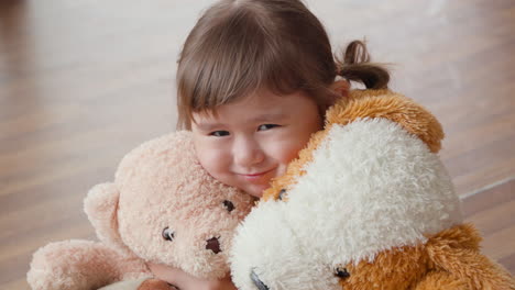 a little girl hugs plush soft toy teddy bears, looking at camera smiling with happiness joy and love to favourite toys - portrait face close-up