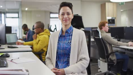 mujer caucásica sentada en el escritorio mirando a la cámara y sonriendo a la cámara en la oficina