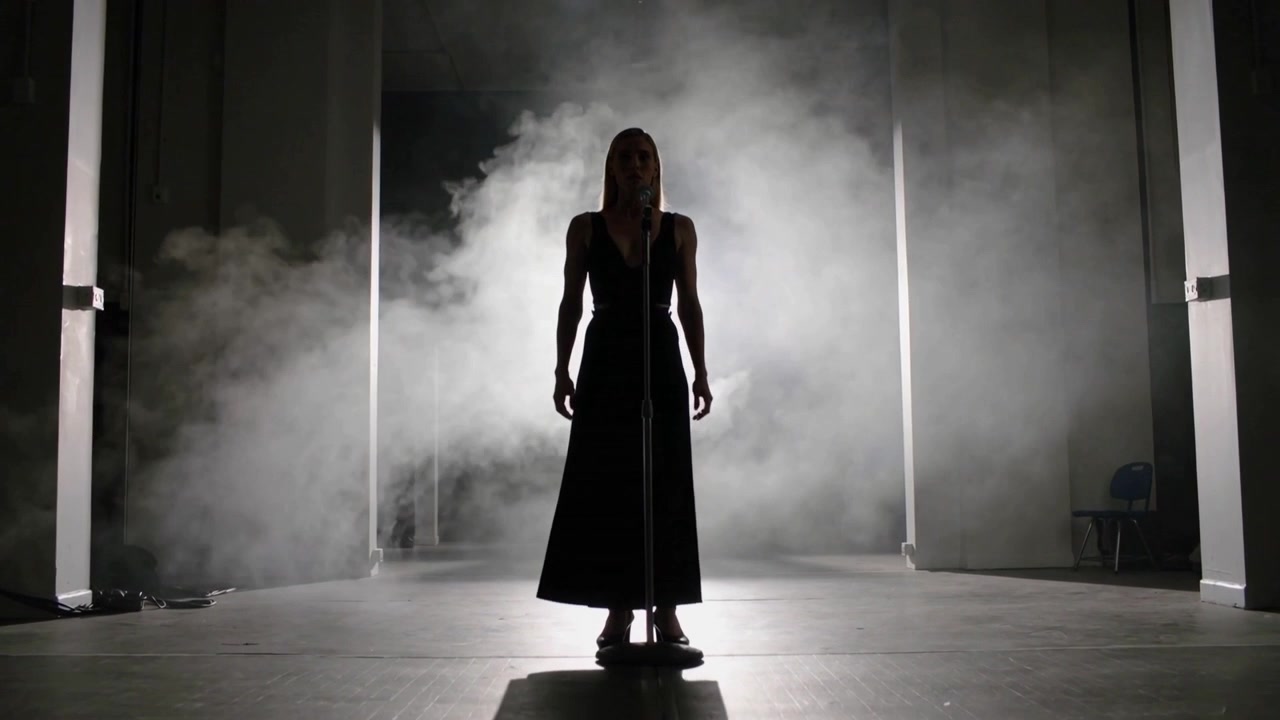 Entering stage right singer in gown walking to midstage mic to sing, backlit fog forming halo