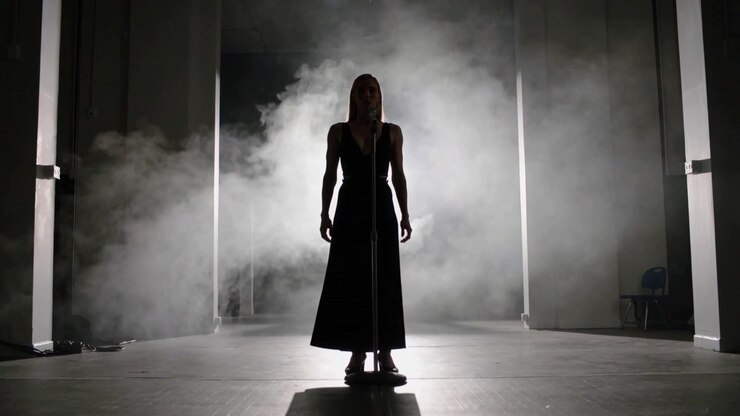 Entering stage right singer in gown walking to midstage mic to sing, backlit fog forming halo