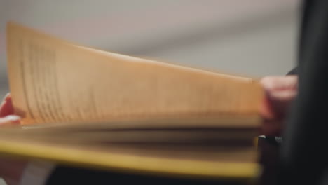 close-up view of hand with well-polished nails adorned with rings gently flipping through pages of book outdoors, wind causes slight resistance as pages turn