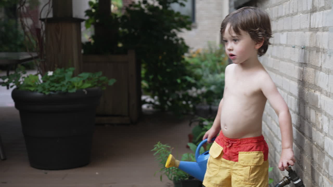 물 스프링클러를 제어하고 아름다운 화창한 날에 푸른 물뿌리개로 식물에 물을 주기 위해 달려가는 어린 소년의 모습