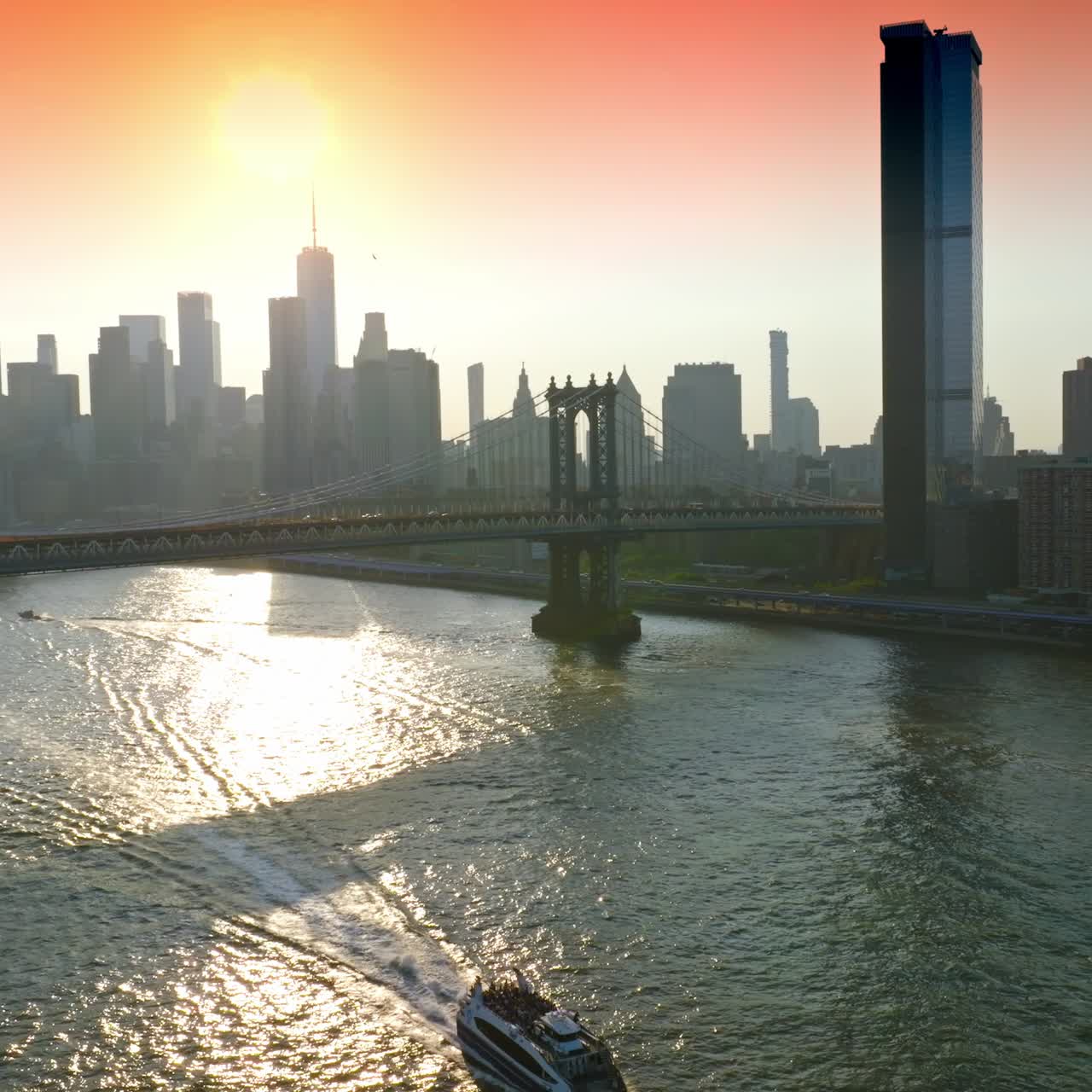 Little boat sailing by East River at sunset. Grey silhouettes of amazing skyscrapers of Manhattan at the backdrop of pink skies
