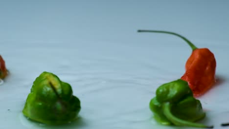 Toma-En-Cámara-Lenta-De-Chiles-Bombay-Rojos-Y-Verdes-Cayendo-En-Un-Charco-De-Agua-Sobre-Una-Superficie-Blanca