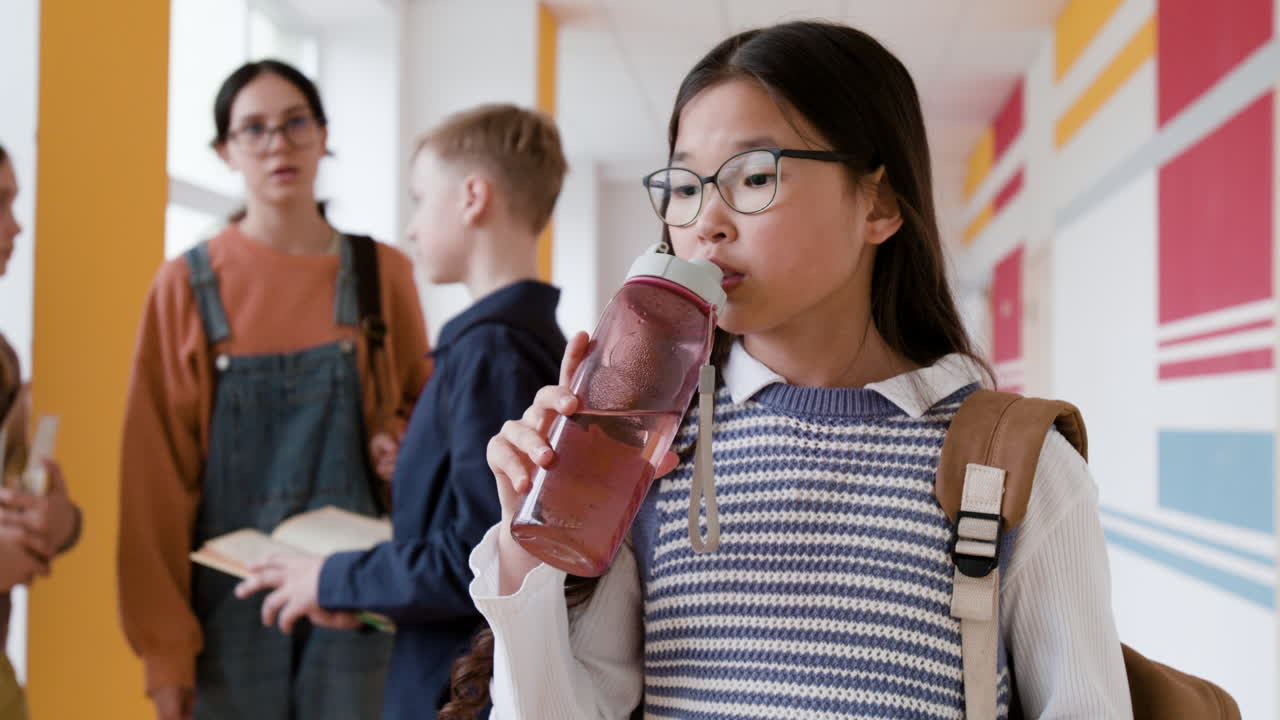Student drinking water from a bottle in a school hallway