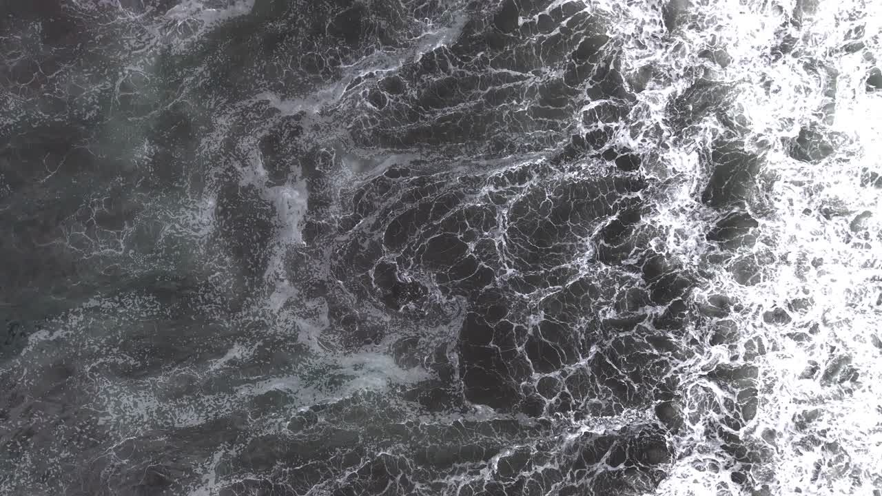 Vista aerea dall'alto verso il basso con drone di onde oceaniche agitate e motivi di schiuma bianca che creano una superficie astratta e текстуizzata in Cile, 4K