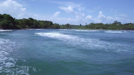 toma aérea de las olas del mar hacia la tierra y los árboles en un día soleado