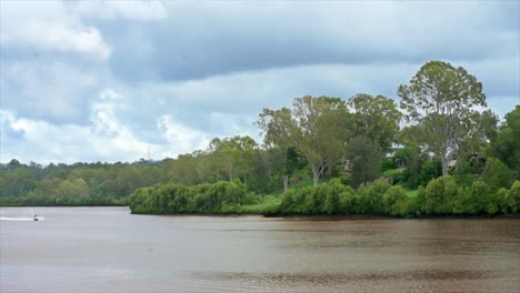 un veloz jetski vuela de izquierda a derecha, en esta hermosa escena fluvial australiana en la selva tropical de queensland