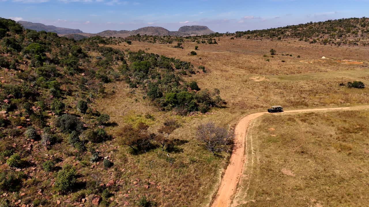 Safari game drive vehicle on dirt road of South African game reserve, aerial