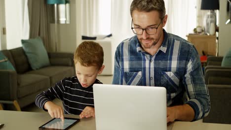 Padre-E-Hijo-Usando-Laptop-Y-Tableta-Digital-En-La-Sala-De-Estar-4k