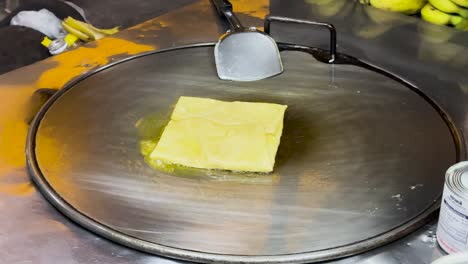 a thai roti sizzles on a hot griddle in phuket, showcasing street food preparation with vibrant lighting and dynamic camera angles