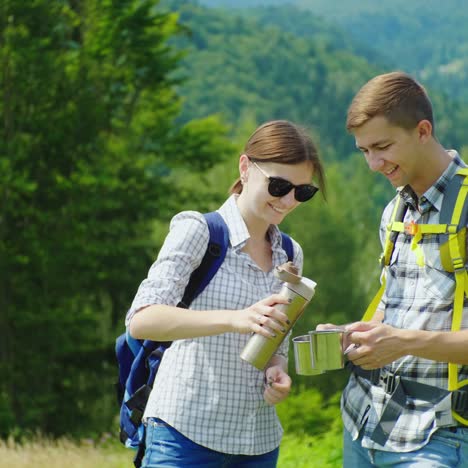 a young couple with backpacks is drinking tea from a thermos bottle