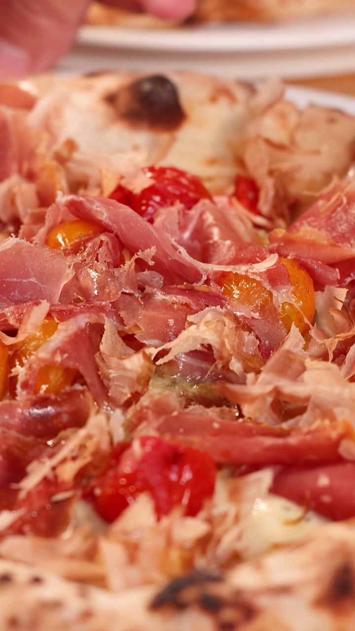 Primo piano di pizza appena sfornata con prosciutto e pomodorini.