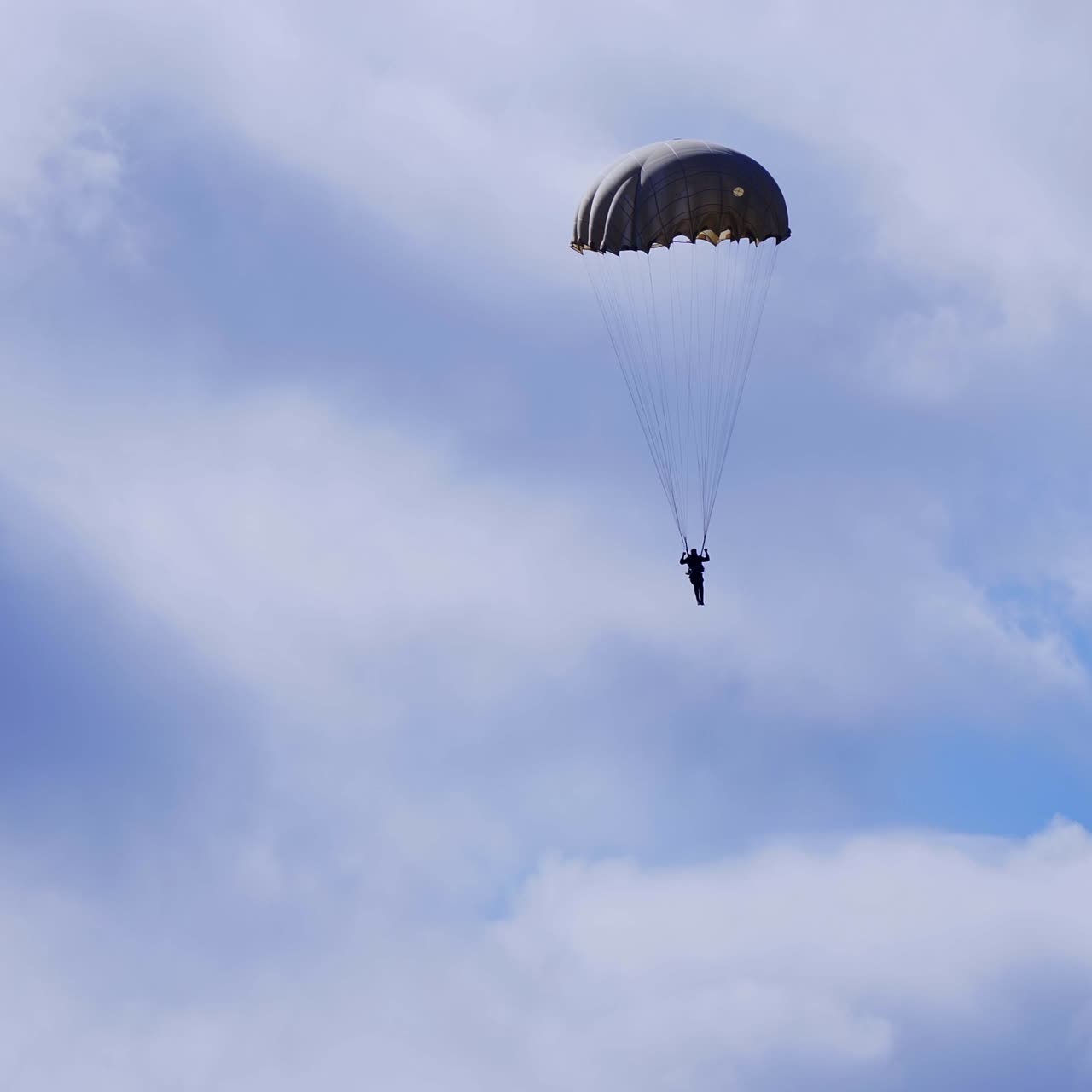 Silhouette of the man with parachute descending to the ground. Parachutist in blue cloudy sky