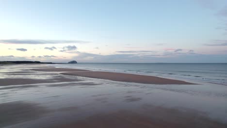 A-drone-facing-out-across-the-calm-ocean-slowly-turns-left-to-reveal-a-subset-reflecting-off-of-a-sandy-beach