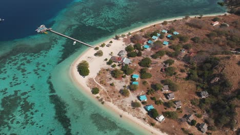 Aerial-drone-shot-of-a-small-island-surrounded-of-amazing-turquoise-ocean-water-with-coral-reefs-and-some-boats-in-the-background