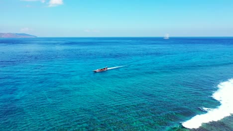 Tourist-boat-sailing-alongside-beautiful-shoreline-of-tropical-island-on-calm-clear-water-of-turquoise-lagoon-in-Bali