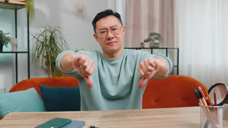 upset chinese man showing thumbs down, dislike bad work, disapproval dissatisfied feedback at home