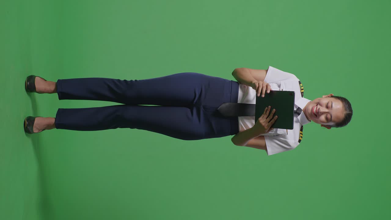 cuerpo lleno de piloto mujer asiática usando una tableta mientras estaba de pie en el estudio de fondo de la pantalla verde