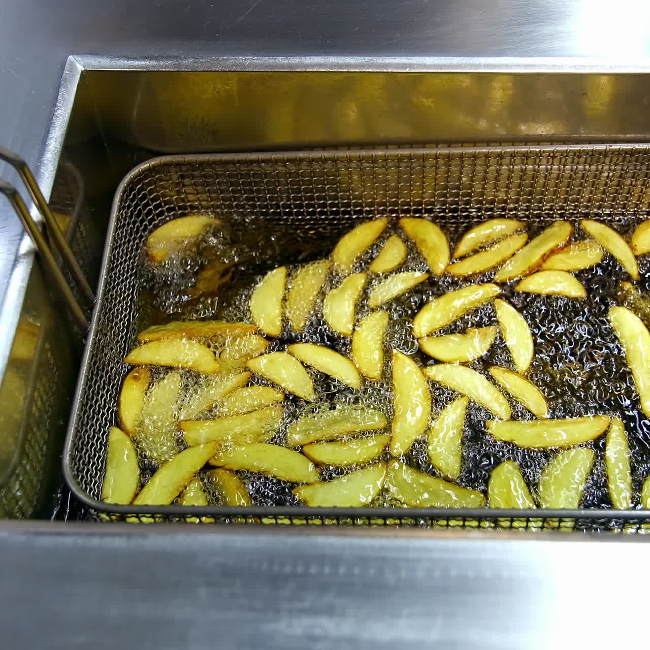 Potato in deep fryer. Crispy fries in the deep fryer in a fast food restaurant. Cooking potato. Junk food concept. Top view. Close up