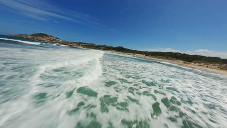 drone fpv volando cerca sobre salpicaduras y olas espumosas y surfear con agua azul clara y cielos a altas velocidades en la playa