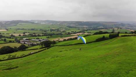 Toma-Aérea-De-Un-Parapente-Que-Llega-A-Tierra-Con-La-Campiña-Inglesa-Detrás