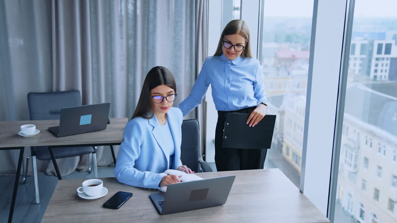 Blonde and dark-haired female employees having conversation in office. Business women look at laptop on the desk discussing some job issues.