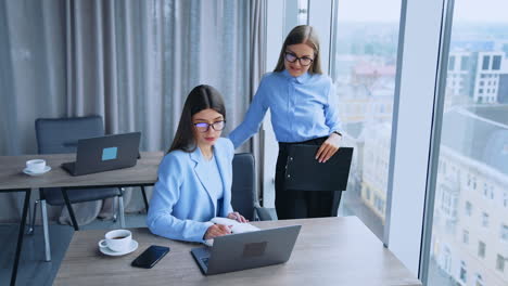 blonde and dark-haired female employees having conversation in office. business women look at laptop on the desk discussing some job issues.