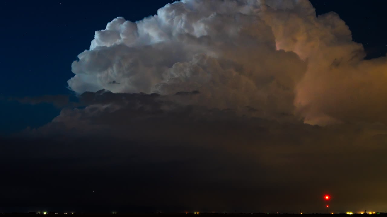 Lightning flashing in a towering storm cloud under starry night sky time lapse