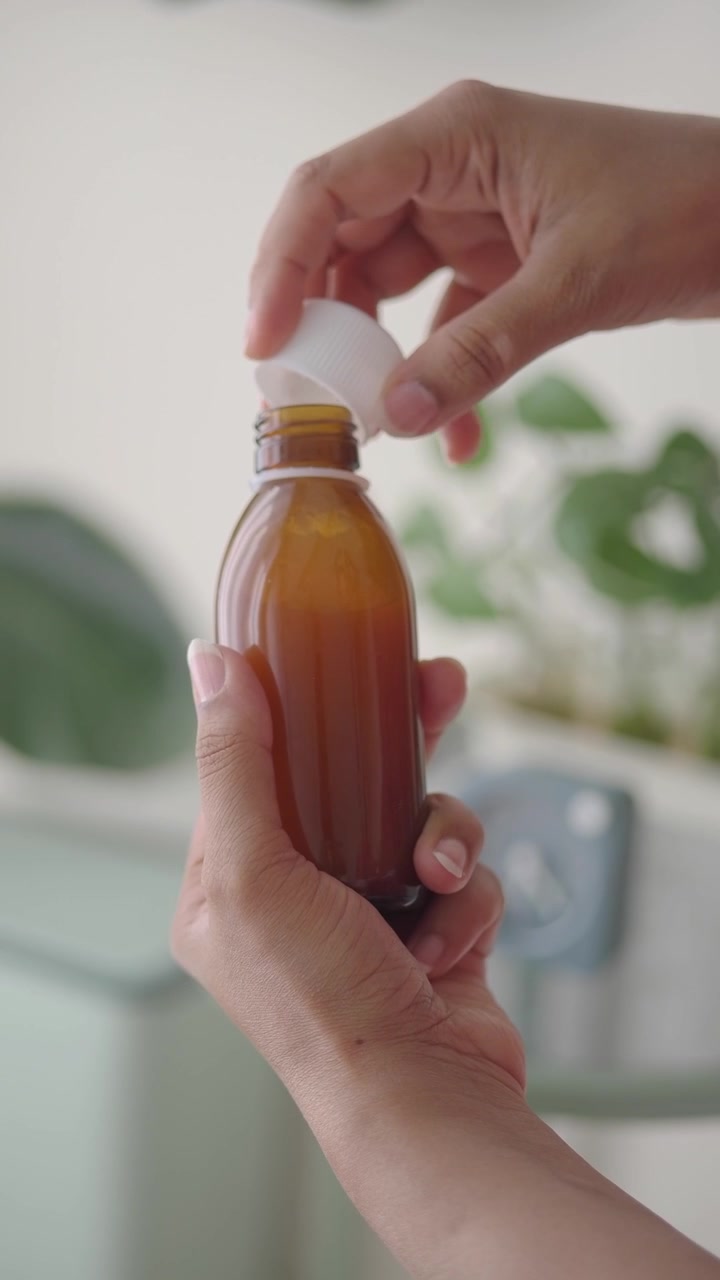 Persona abriendo una pequeña botella ámbar de líquido