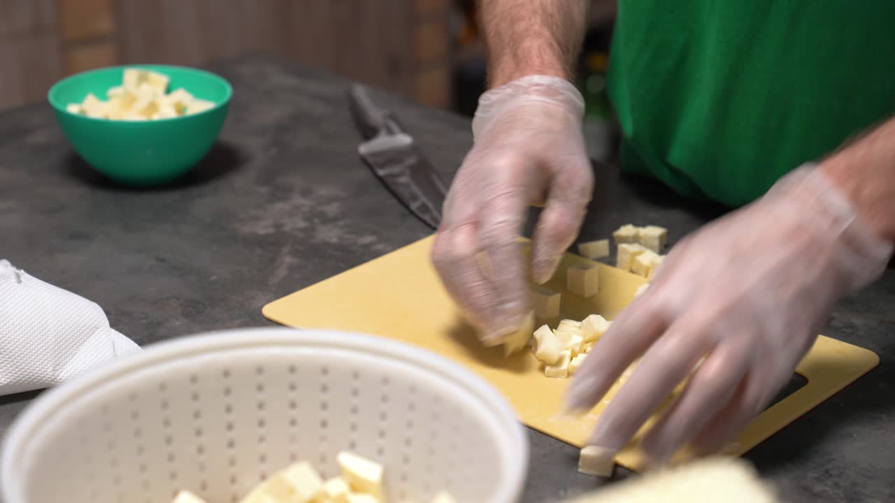 Persona con i guanti che prepara il cibo, tagliando un blocco di formaggio bianco o tofu a cubetti.