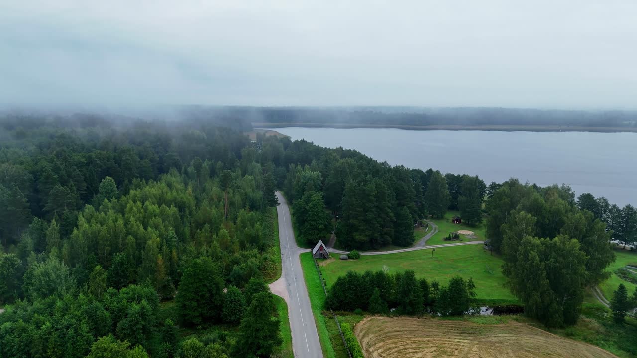 Drone footage of Usma Lake with forests, fields, and a long straight road leading to the water