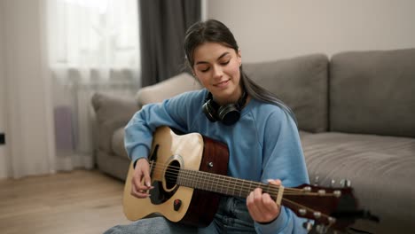 young girl learning to play the guitar, sitting on the floor in headphones