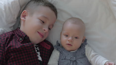 boy and his baby sister lying on a bed