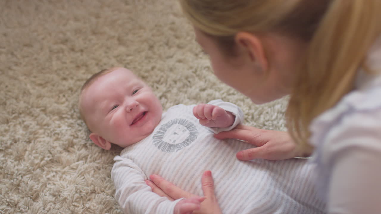 Loving mother playing game and tickling baby son lying on rug in child's bedroom at home - shot in slow motion