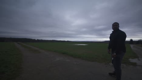 Modern-Black-Swordsman-Warrior-Awaiting-Battle-Opponent-in-Open-Field-Under-Grey-Sky,-Europe,-4K-|-Muscular,-Intimidating,-Shadow,-Figure,-Blurry,-Dark-Clothes,-Powerful,-Thinking,-Moving-Fight-Stance