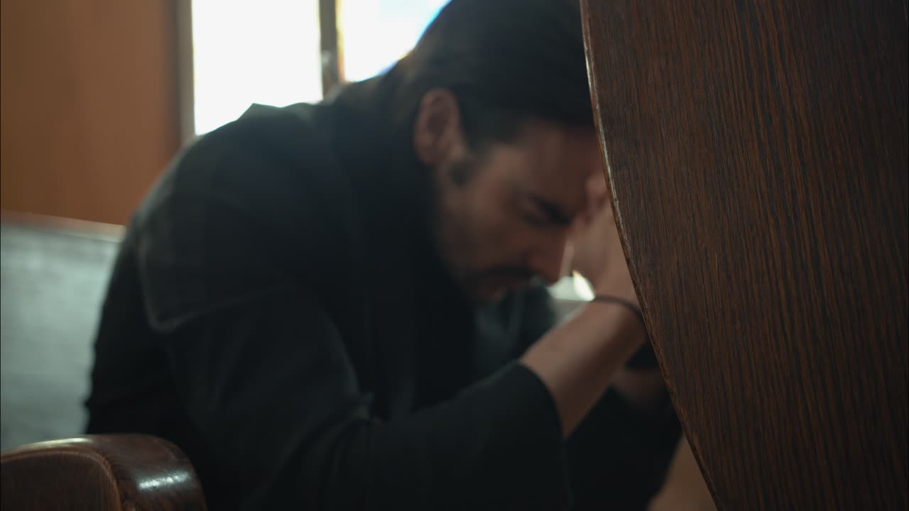 검은색 슈트를 입은 젊은이가 영화 속도 느린 동작으로 교회에서 기도하고 있습니다.