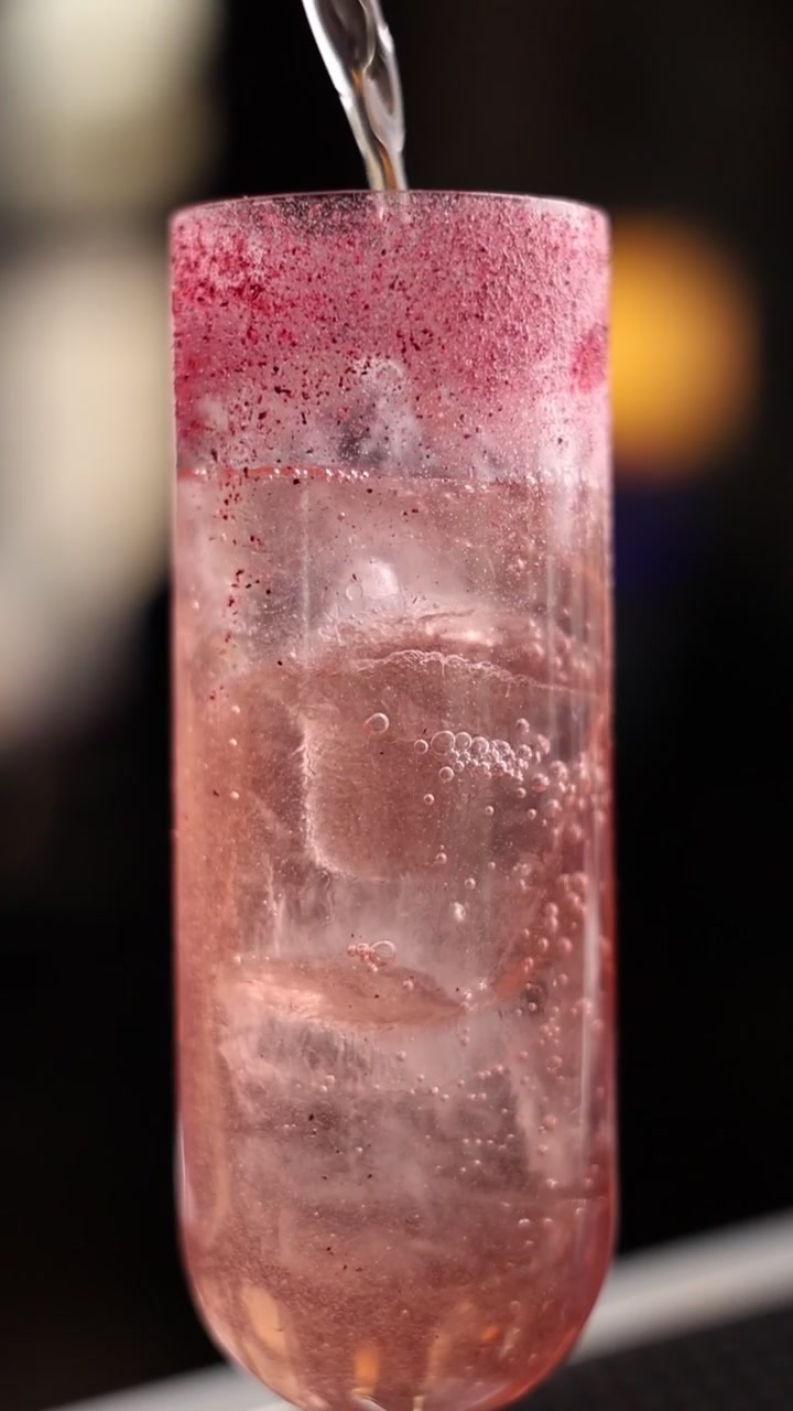 Liquido trasparente versato in un bicchiere da cocktail rosa con ghiaccio