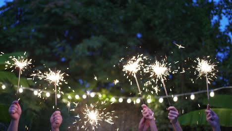 patio party. the hands of different people hold sparklers. new year in the tropics. friends dancing and having fun