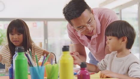 asian father having fun with children doing craft on table at home