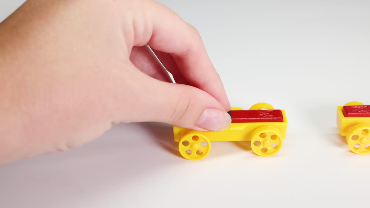 Hands manipulate colorful magnetic toy cars on a white surface, illustrating magnetic attraction and repulsion in a playful setting