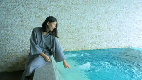 The-soft-and-blur-focus-of-Asia-women-sitting-on-private-poolside-in-the-resort-and-use-her-hand-to-splashing-the-water-on-vacation-time