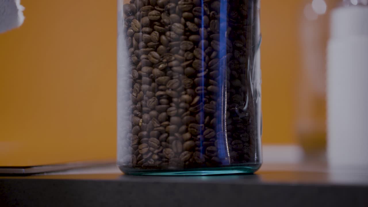 Beautiful brown coffee beans in a glass jar with yellow background